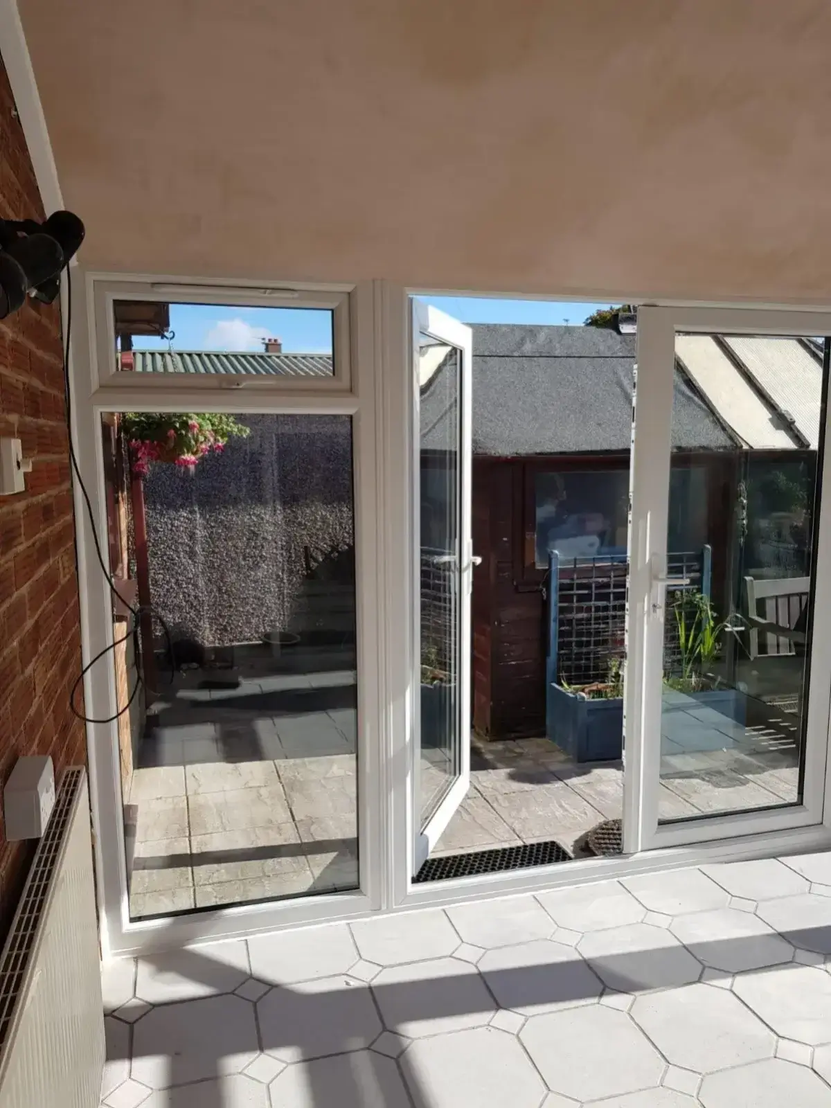 Clean internal perspective looking through open conservatory French doors out to a manicured garden space. Work by Norfolk Exterior Solutions